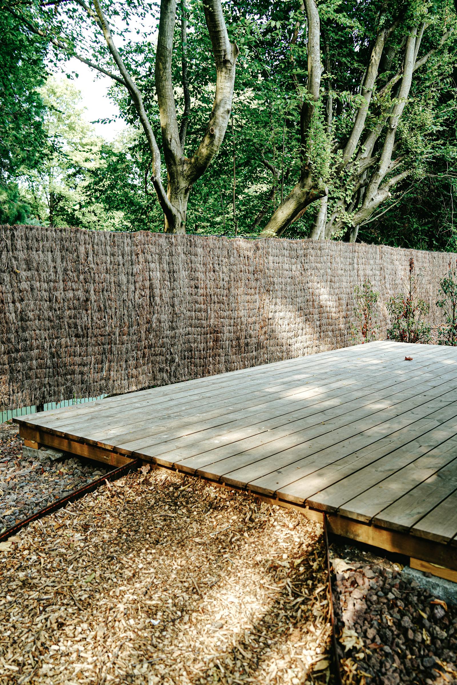 Clean restored wooden deck surrounded by lush green trees and privacy fence