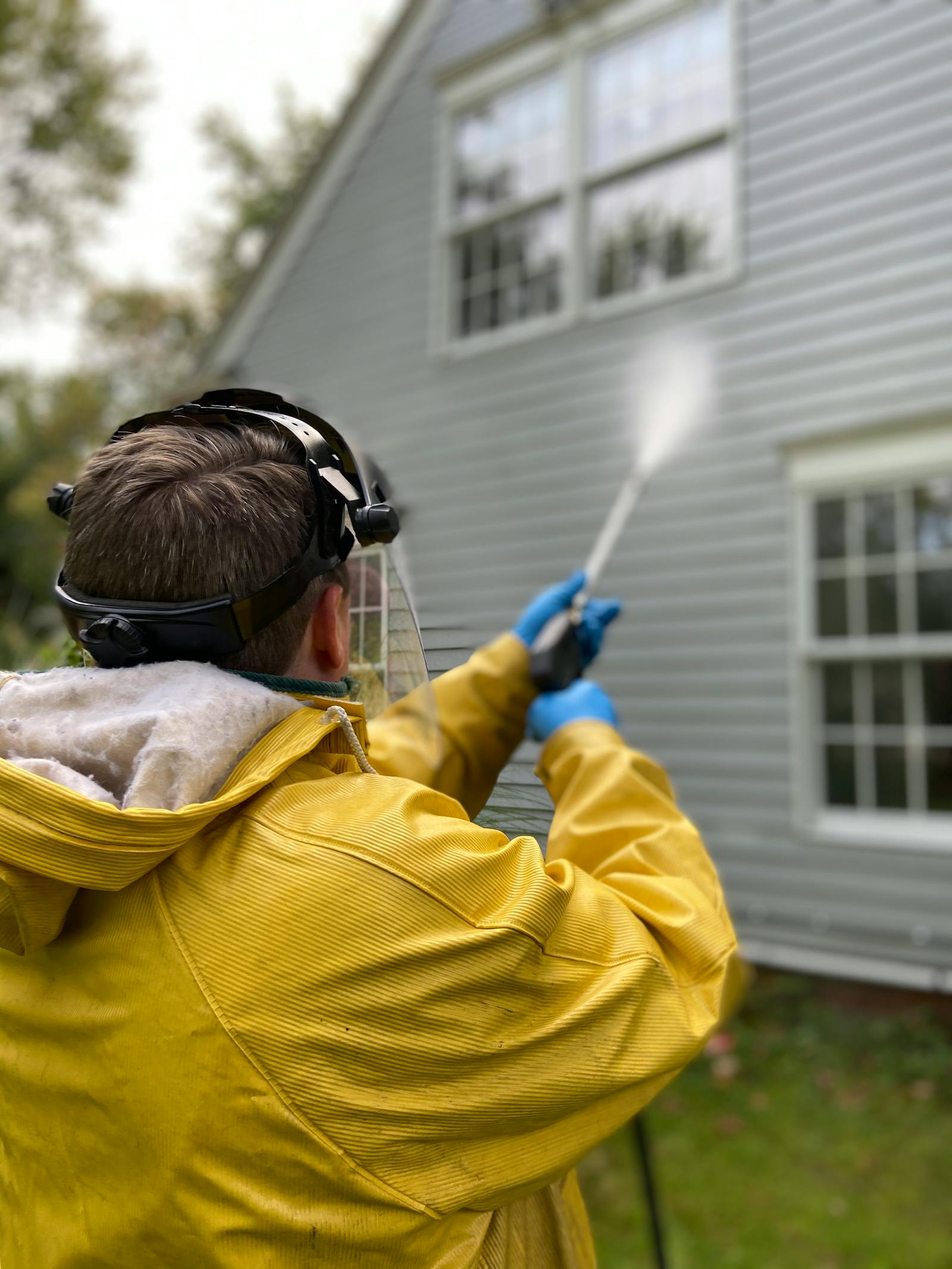 Technician pressure washing dingy house siding before cleaning